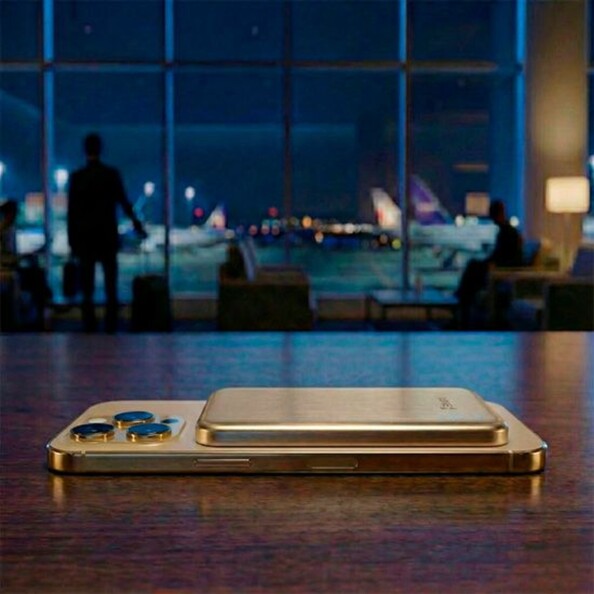 Mise en situation d'un smartphone Android avec batterie externe posée dessus sur une table en bois dans un grand hall d'un aéroport avec baie vitrée donnant sur les pistes d'atterrissage de nuit