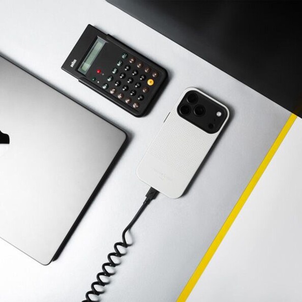 Mise en situation du branchement du câble rétro spirale USB-C vers USB-C à un téléphone portable posé sur l'écran sur une table à côté d'un PC portable fermé et d'une calculatrice