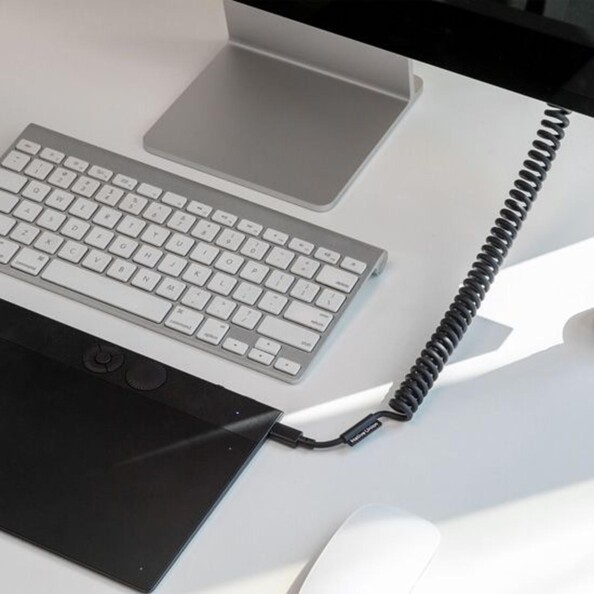 Mise en situation du branchement du câble rétro spirale USB-C vers USB-C à une tablette éteinte à côté d'un clavier sans fil et d'un PC type Mac
