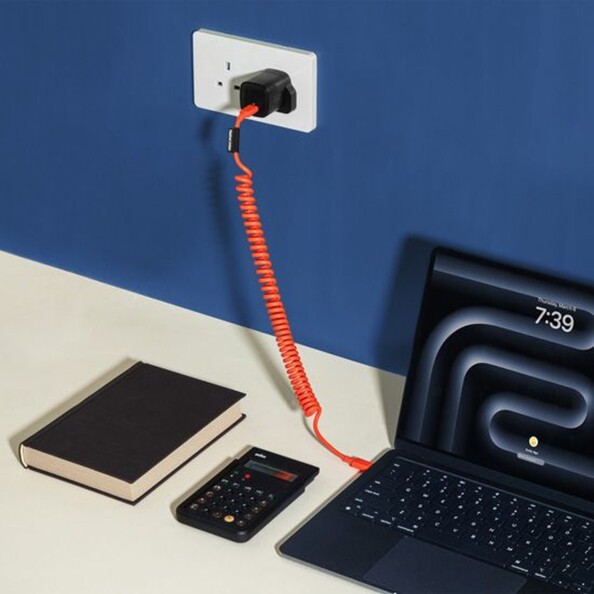 Mise en situation du branchement du câble rétro spirale USB-C vers USB-C à un PC portable et à une prise secteur murale à côté d'une calculatrice et d'un livre