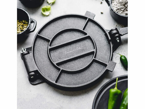 Presse à tortillas ronde en fonte noire, entourée de bols avec graines et farine, piments verts
