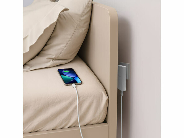 Chargeur secteur plat USB-A / USB-C 30 W mis en situation derrière une tête de lit chargeant un smartphone