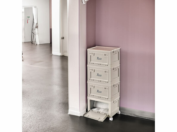 Mise en situation de quatre boîtes de rangement empilées sur quatre roues et installées dans un coin