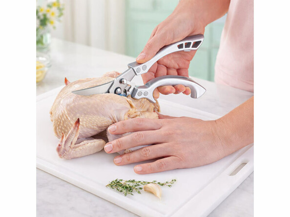 Ciseaux à volaille en acier inoxydables mis en situation entrain de découper un poulet sur un plan de travail