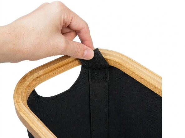 Main fixant la languette velcro noire sur le cadre en bois clair du panier Infactory