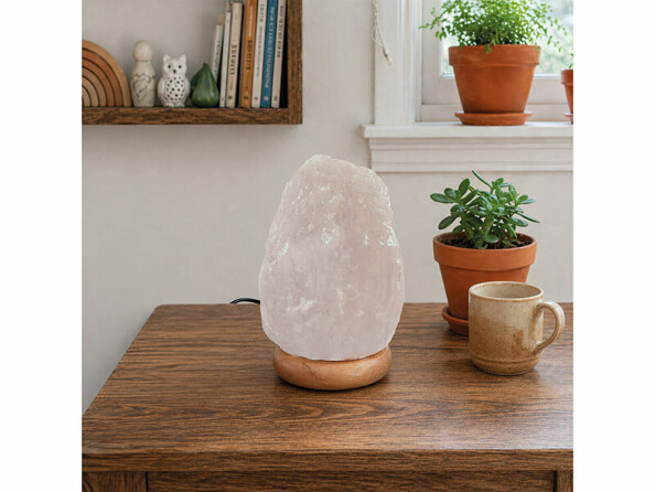 Lampe de sel blanche sur base en bois, sur une table, à côté d’une tasse beige et d’une plante verte en pot