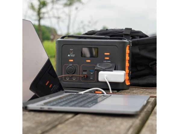 Mise en situation du chargement d'un PC portable par chargeur secteur branché à la prise secteur de la batterie portative sur une table en bois en extérieur