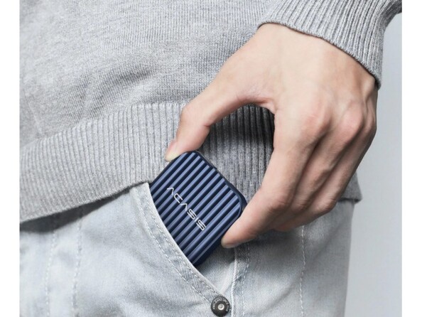 Main d'homme habillé en gris glissant le boîtier en aluminium bleu pour SSD M.2 2230 dans la poche gauche de son jean