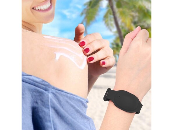 Application de crème solaire sur l'épaule d'une femme assise sur la plage avec le bracelet distributeur autour du poignet