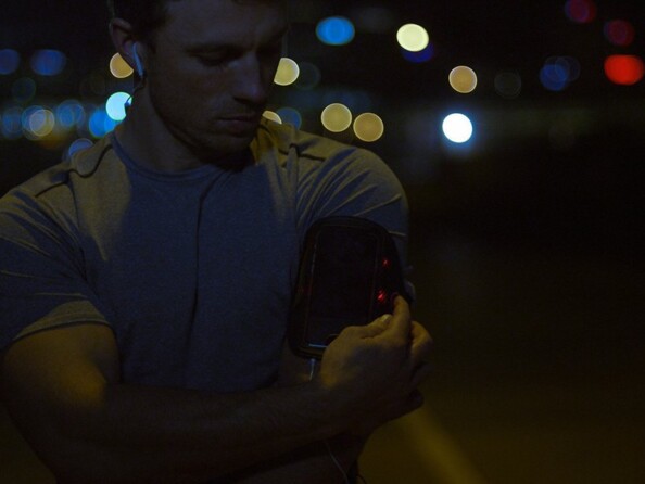 Homme sportif musclé réglant le brassard à scratch pour smartphone autour de son bras avant sa séance de sport nocturne