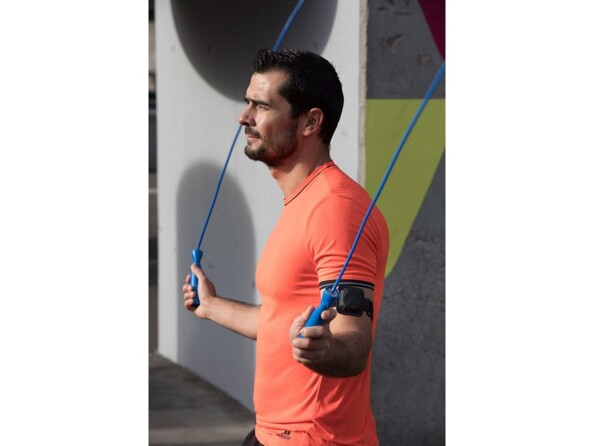 Homme en t-shirt orange fluo en séance de musculation avec tendeurs et brassard au biceps gauche