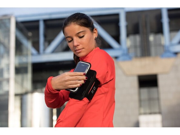 Jeune femme en survêtement fluo fixant de la main gauche son téléphone sur son brassard aimanté sur son biceps gauche avant d'aller courir