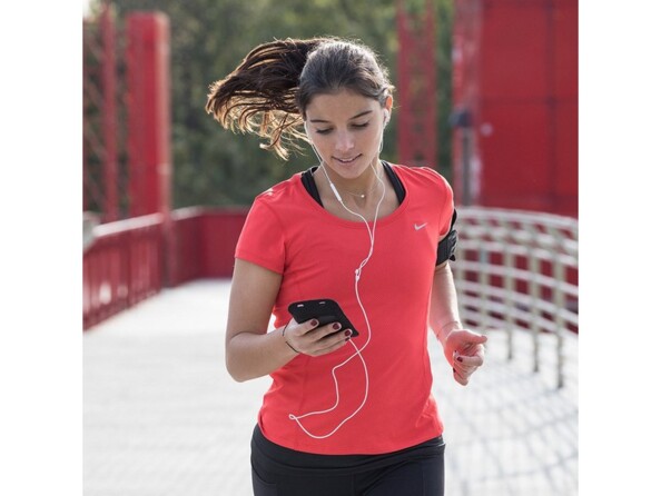 Jeune femme entrain de courir sur un pont avec les écouteurs filaires dans les oreilles et son smartphone à la main