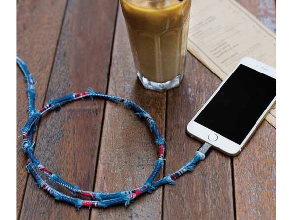 Branchement du câble Lightning en jean denim au port de chargement Lightning d'un iPhone à côté d'un verre rempli de boisson