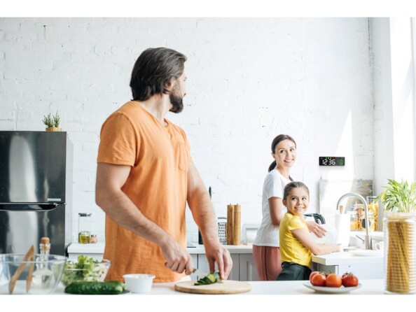 Mise en situation d'une famille de deux parents avec enfant faisant la cuisinre avec le détecteur de CO2 fixé au mur