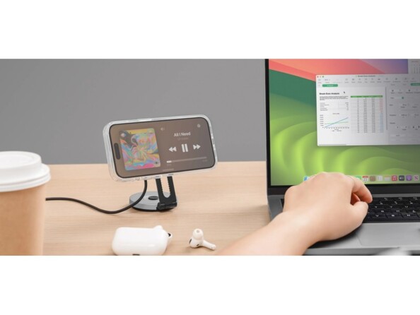 Mise en situation d'un smartphone en cours de chargement fixé à l'horinzontale sur la surface à induction du chargeur Orbit Pro à côté d'un gobelet en carton et d'un PC portable sur lequel une personne travaille