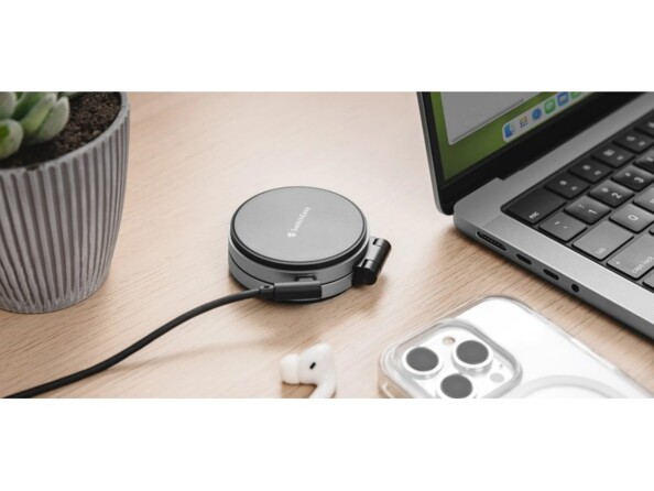Mise en situation du chargement du chargeur à induction Qi2 rond replié par câble USB-C sur un bureau en bois, à côté d'un PC portable, d'une plante grasse et d'un iphone retourné