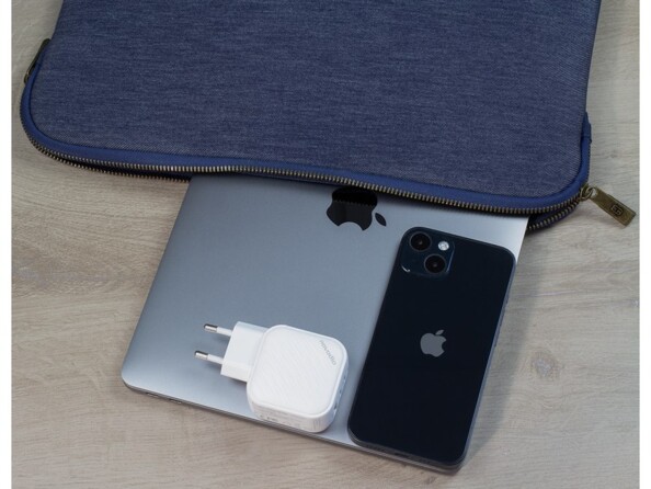 Mise en situation de l'adaptateur secteur USB-C/USB-A posé sur un MacBook sorti de sa sacoche de protection à côté d'un iPhone