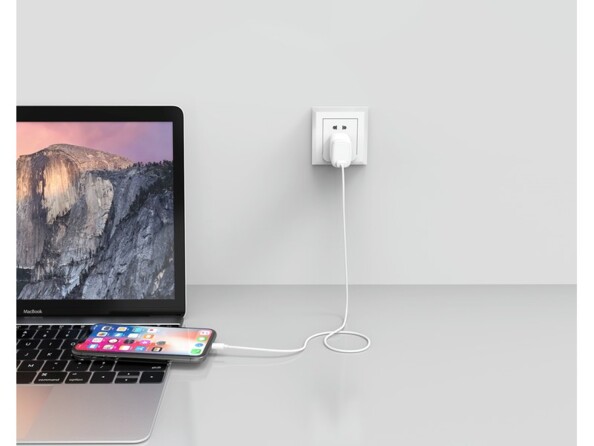 Mise en situation de l'adaptateur secteur Novodio coloris blanc branché à une prise de courant et à un iPhone allumé lui-même posé sur un MacBook