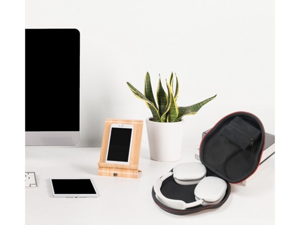 Mise en situation d'un casque AirPods Max avec coque de protection rigide posé sur un meuble en blanc à côté d'un PC, d'une plante verte et d'un smartphone sur support