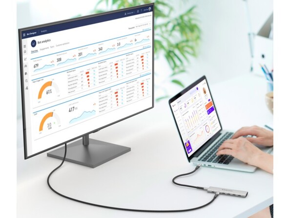 Configuration de bureau multi-écrans avec écran PC fixe raccordé par hub et câbles USB-C à un PC portable sur lequel une personne travaille dessus