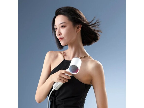 Femme asiatique trentenaire en robe noire et dorée se séchant ses cheveux bruns à la coupe au carré par en dessous en tenant le sèche cheveux blanc Roidmi Miro dans sa main droite