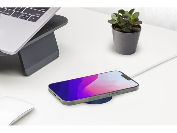 Chargement sans fil par induction d'un chargeur secteur MagSafe avec étui en silicone bleu sur un bureau à côté d'une plante grasse et d'un PC portable