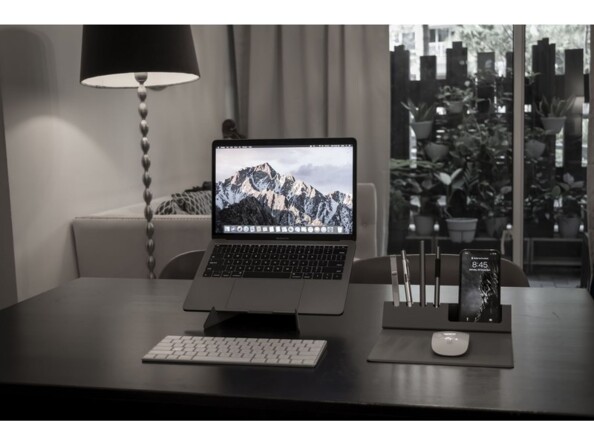 Setup moderne dans un building type loft new-yorkais avec PC portable sur support, clavier sans fil et pad avec souris sans fil, smartphone et stylos organisés