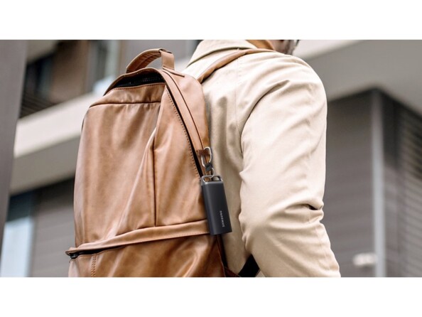 Mise en situation du SSD externe portable Samsung fixé à la tirette d'un sac à dos brun porté par un jeune homme en extérieur