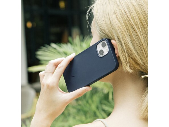 Jeune femme blonde les cheveux attachés en queue de cheval téléphonant avec son iPhone protégé par une coque couleur noire à l'oreille en extérieur