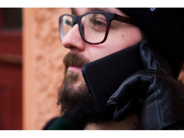 Homme trentenaire barbu à lunettes avec manteau, bonnet et gants téléphonant à l'extérieur avec son iPhone à l'oreille