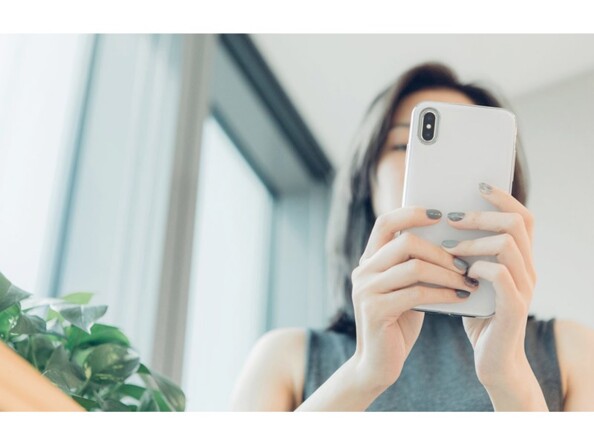 Jeune femme en débardeur tenant son iphone devant son visage à deux mains