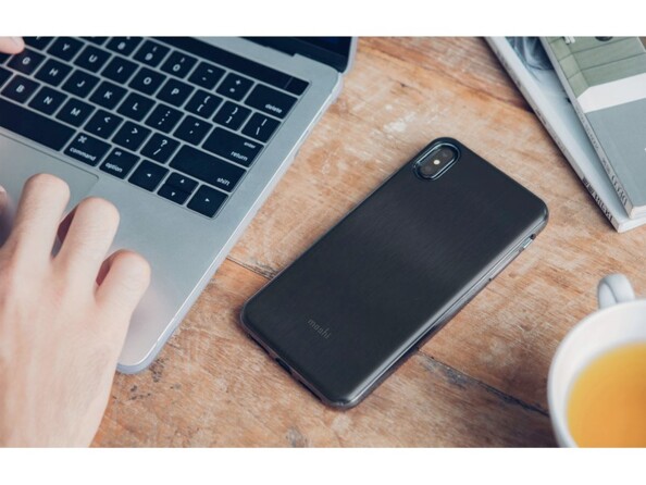 iPhone avec housse rigide et souple couleur noire posé sur l'écran tactile à côté d'une tasse de thé et d'un PC portable sur lequel une personne travaille