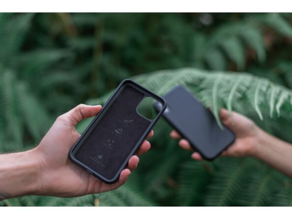 Aperçu de l'intérieur en tissu et de l'extérieur rigide de la coque recyclable et biodégradable coloris noir dans deux mains tendues devant des fougères