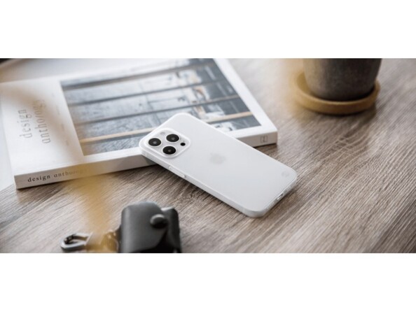 Mise en situation d'un iphone 13 Pro avec coque blanche transparente posée de biais sur un livre sur un bureau en bois