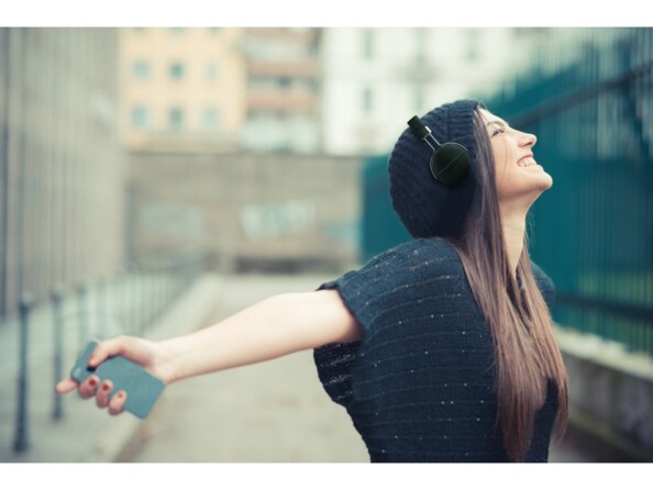 Jeune femme en t-shirt les bras ouverts et le regard vers le ciel écoutant de la musique en streaming dans la rue