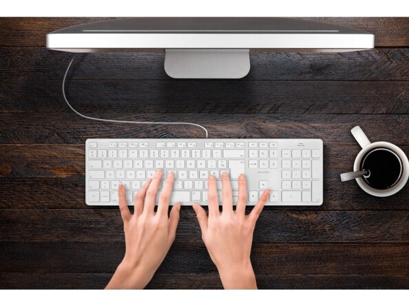 Mise en situation d'une personne tapant à deux mains sur le clavier Novodio Touch Keyboard USB-C branché à un Mac à côté d'une tasse de café sur un bureau en bois foncé