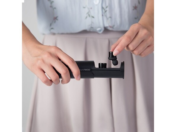 Mise en place des oreillettes Swarmoo Cosy Pro dans leur boîtier de chargement cylindrique par une femme en jupe