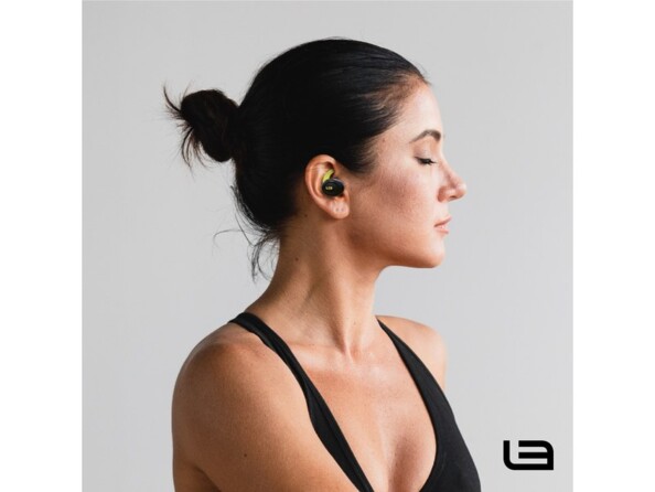 Jeune femme sportive en débardeur noir avec cheveux attachés en chignon, les yeux fermés et écoutant de la musique sans fil via une oreillette