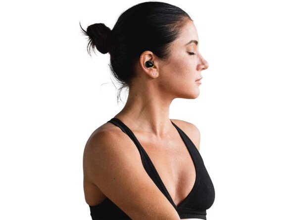 Jeune femme sportive en débardeur noir avec cheveux attachés en chignon, les yeux fermés et écoutant de la musique sans fil via une oreillette