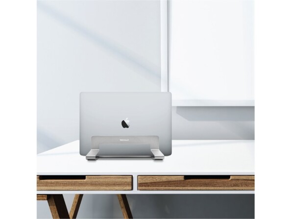 MacBook gris clair rangé fermé dans le support MacAlly en acier couleur aluminium sur une table scandinave minimaliste coloris blanc et bois devant une fenêtre