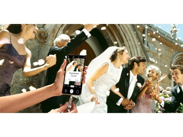 Insertion de la clé USB-C 2 en 1 Sandisk dans le port d'un smartphone affichant un message d'erreur lié à l'espace de stockage pendant qu'il immortalise un mariage homme/femme à la sortie de l'église