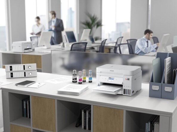 Mise en place de l'imprimante ET-4856 Epson EcoTank sur un meuble à côté d'une ramette de papier et 4 bouteilles d'encre au milieu d'un open space