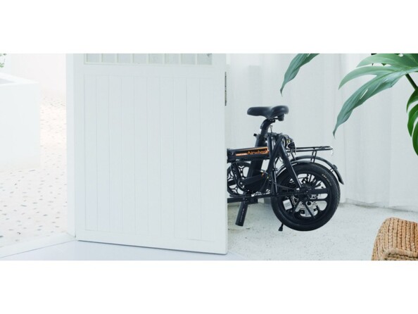 Mise en situation du vélo de ville à assistance électrique plié derrière un portail et une clôture en bois blanc