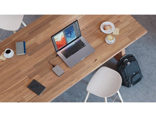 Mise en situation du disque dur externe LaCie Mobile Drive branché à un PC portable allumé sur une table en bois à côté d'un petit déjeuner et d'autres affaires de bureau