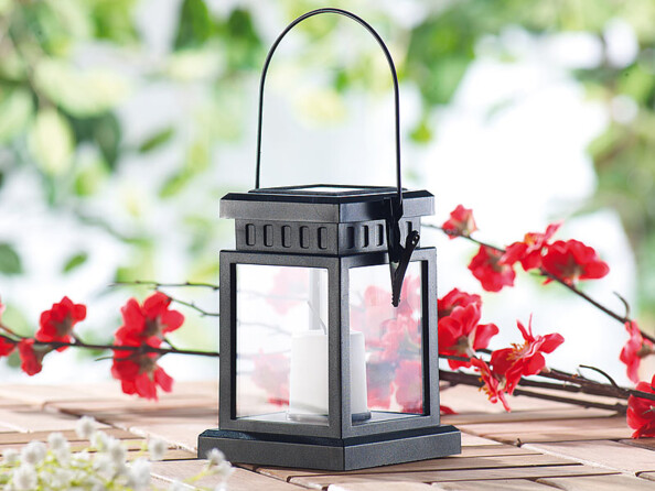 Lanterne asiatique noire contenant une fausse bougie blanche à LED posée sur une table à côté de fleurs rouges