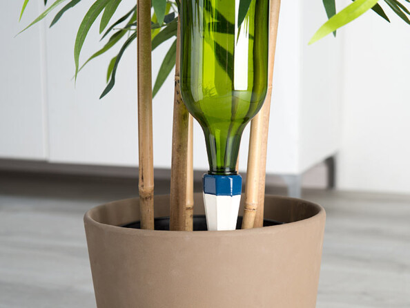 Zoom sur l'adaptateur avec bouteille en plastique fixé dessus dans un pot de fleur couleur taupe avec plante