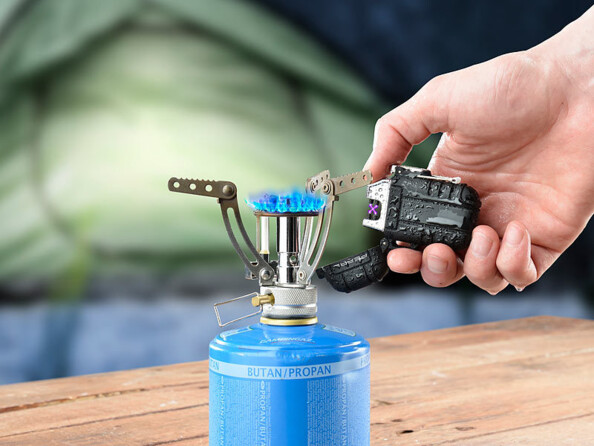 Main allumant un réchaud de camping à gaz avec le briquet plasma noir à double arc, arc violet allumé