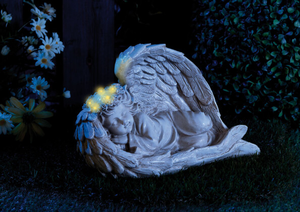 Ange avec couronne lumineuse allumée de nuit posé dans un jardin