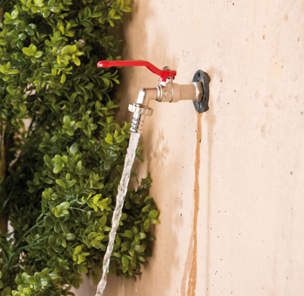 Mise en situation du robinet 1/2" avec vanne quart de tour rouge fixé à un mur extérieur et délivrant de l'eau